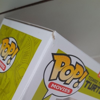 Caixa Funko Pop! Movies branca com amassadura e texto 'POP! MOVIES' e 'TEENAGE MUTANT TURTLES'.