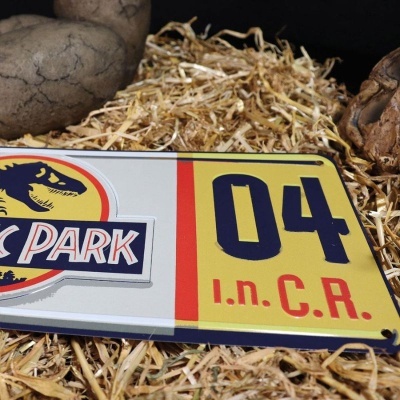 Placa metálica Jurassic Park com números e letras sobre palha