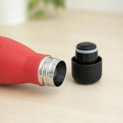 Garrafa térmica vermelha com tampa preta removida sobre mesa de madeira clara