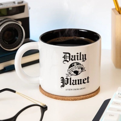 Caneca branca com texto Daily Planet sobre mesa com câmara, óculos e canetas