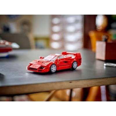Miniatura de carro desportivo vermelho feito de blocos de construção com rodas cinza e logótipo Ferrari numa mesa cinza.