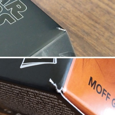 Cantoneiras danificadas de embalagens preta e ferrugem com texto parcial visível.