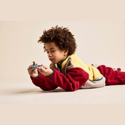 Criança deitada a brincar com brinquedo, vestindo casaco colorido de fleece