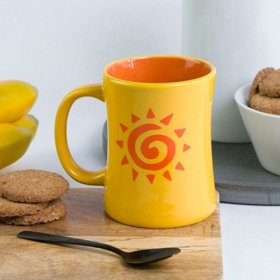 Caneca amarelo com desenho de sol vermelho, bolachas, colher preta e bananas