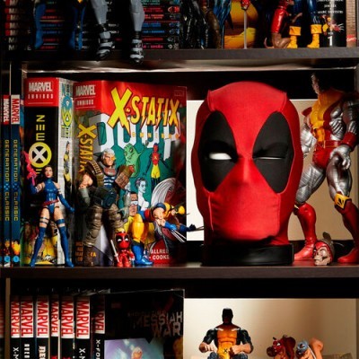 Estante com livros e figuras de ação Marvel, destaque para cabeça grande de Deadpool e figuras de Wolverine.