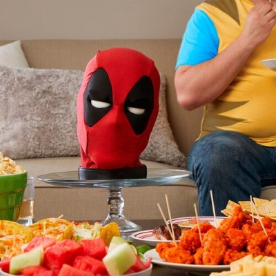 Máscara de Deadpool vermelha e preta sobre suporte numa mesa com petiscos e frutas