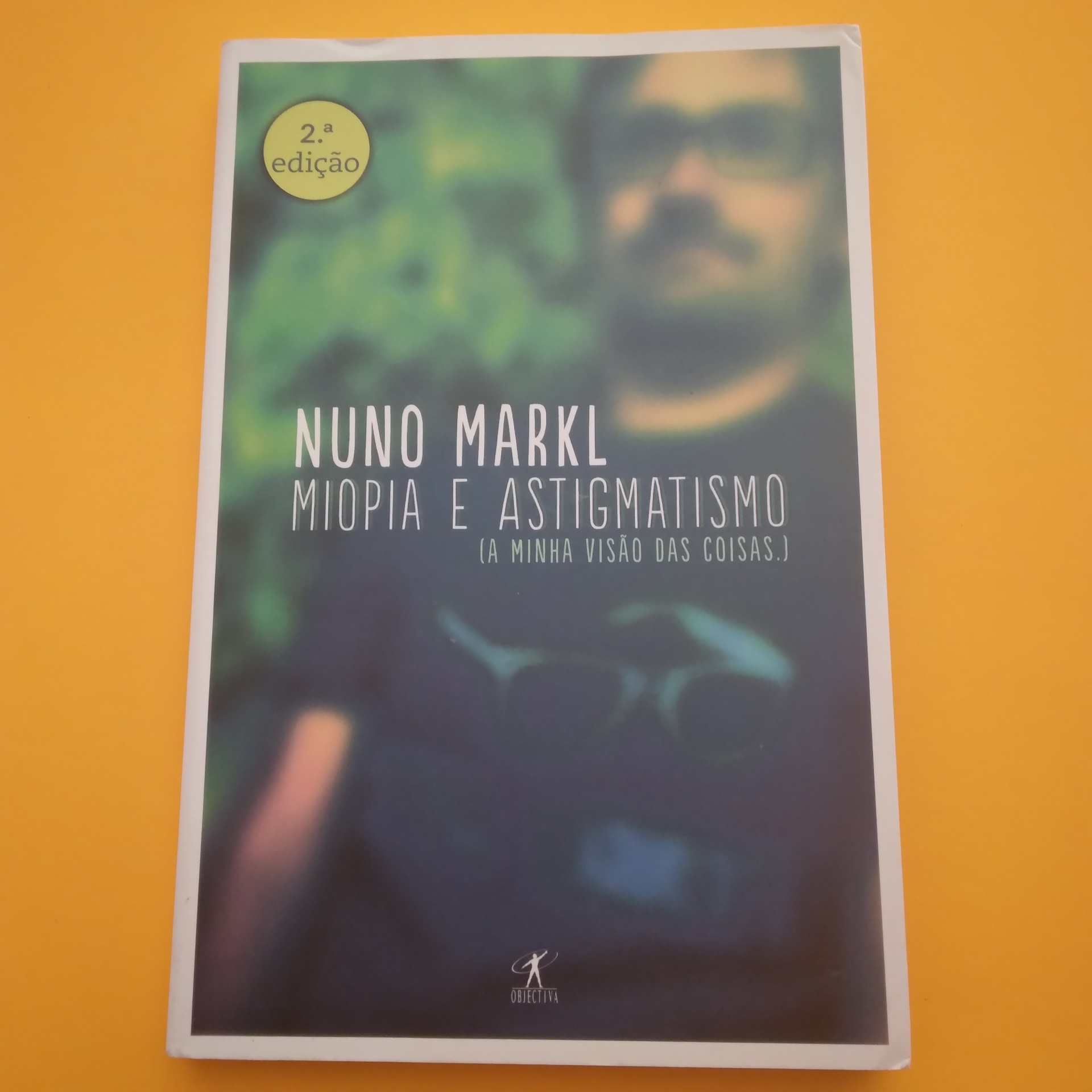 Miopia e Astigmatismo, Nuno Markl Livro 'Miopia e Astigmatismo' de Nuno Markl sobre fundo desfocado com imagem de homem