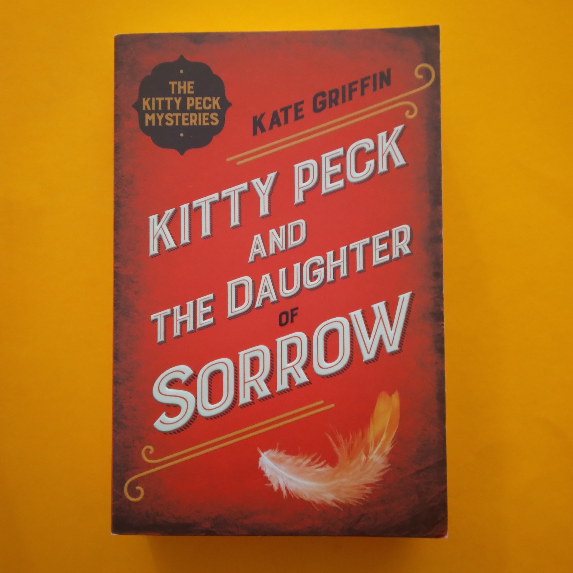 Kitty Peck and the Daughter of Sorrow, Kate Griffin Livro 'Kitty Peck and the Daughter of Sorrow' com capa vermelha e pena desenhada