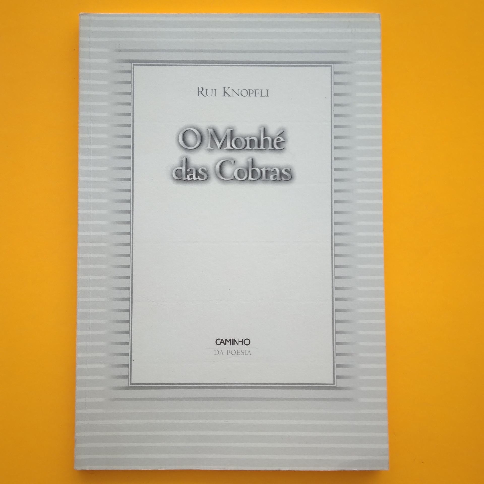 O Monhé das Cobras, Rui Knopfli Capa de livro branco com título 'O Monhé das Cobras' sobre fundo amarelo