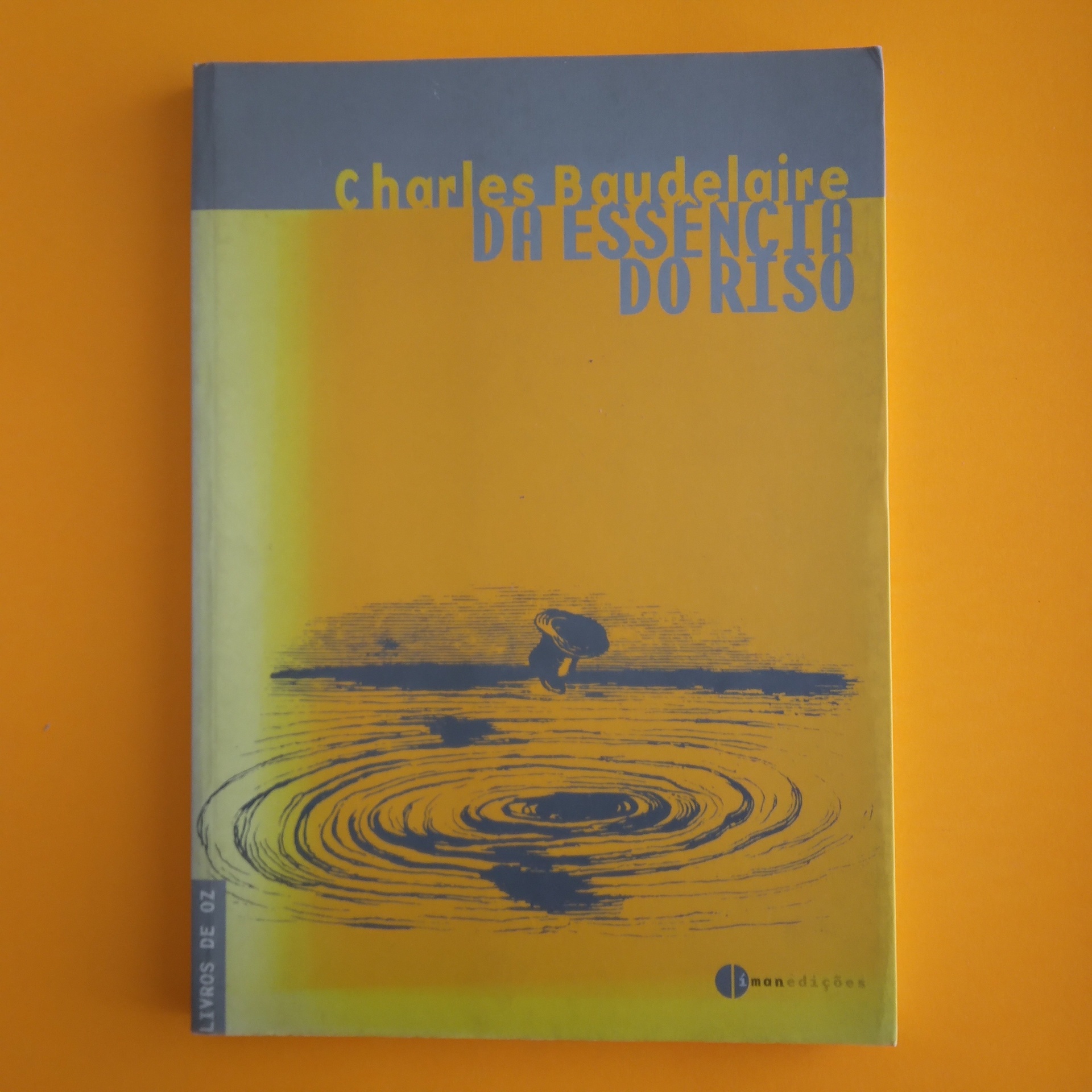 Da Essência do Riso, Charles Baudelaire Capa de livro amarela com texto azul e ilustração de pessoa junto a água.
