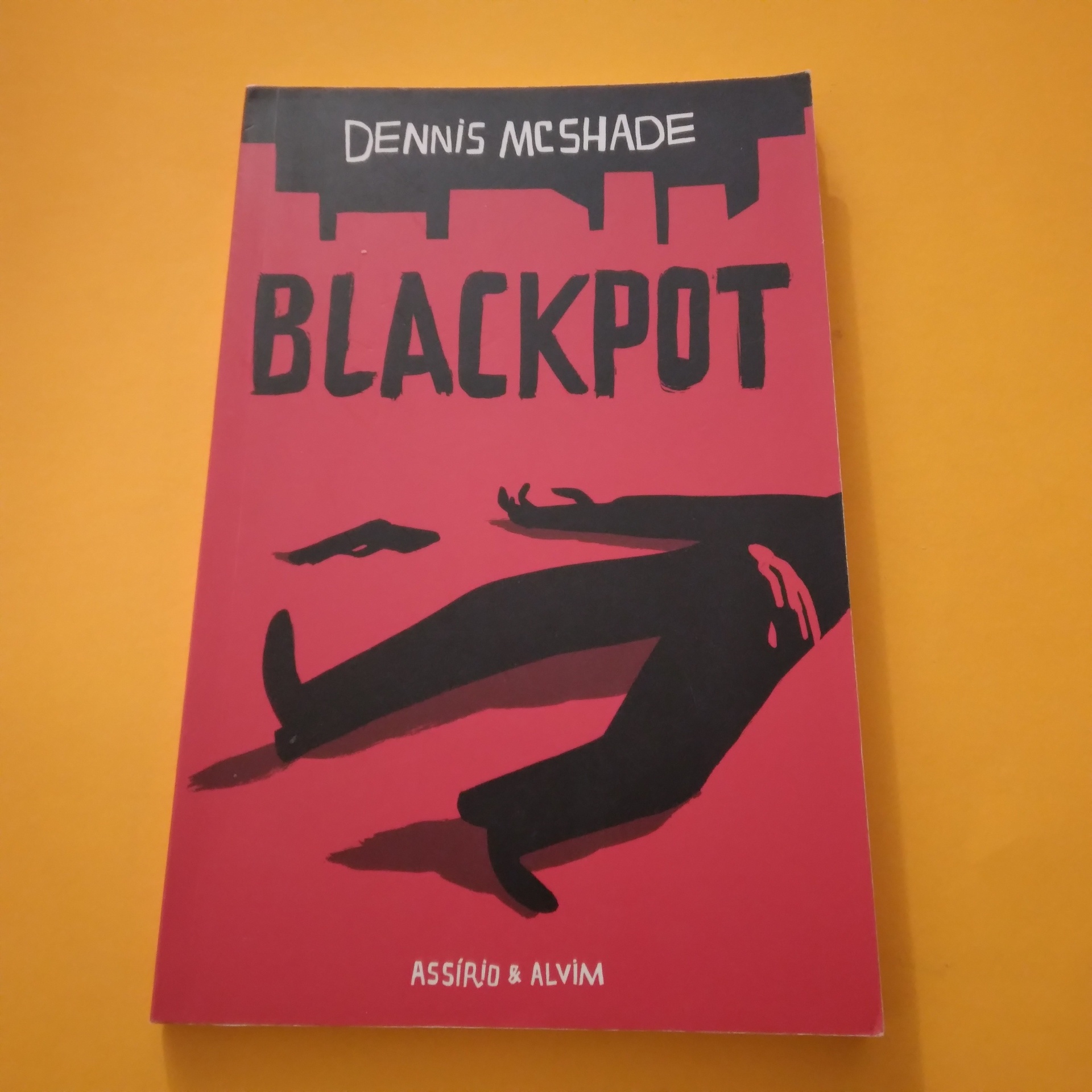 Blackpot, Dennis McShade Livro BLACKPOT com capa vermelha e preta sobre fundo laranja