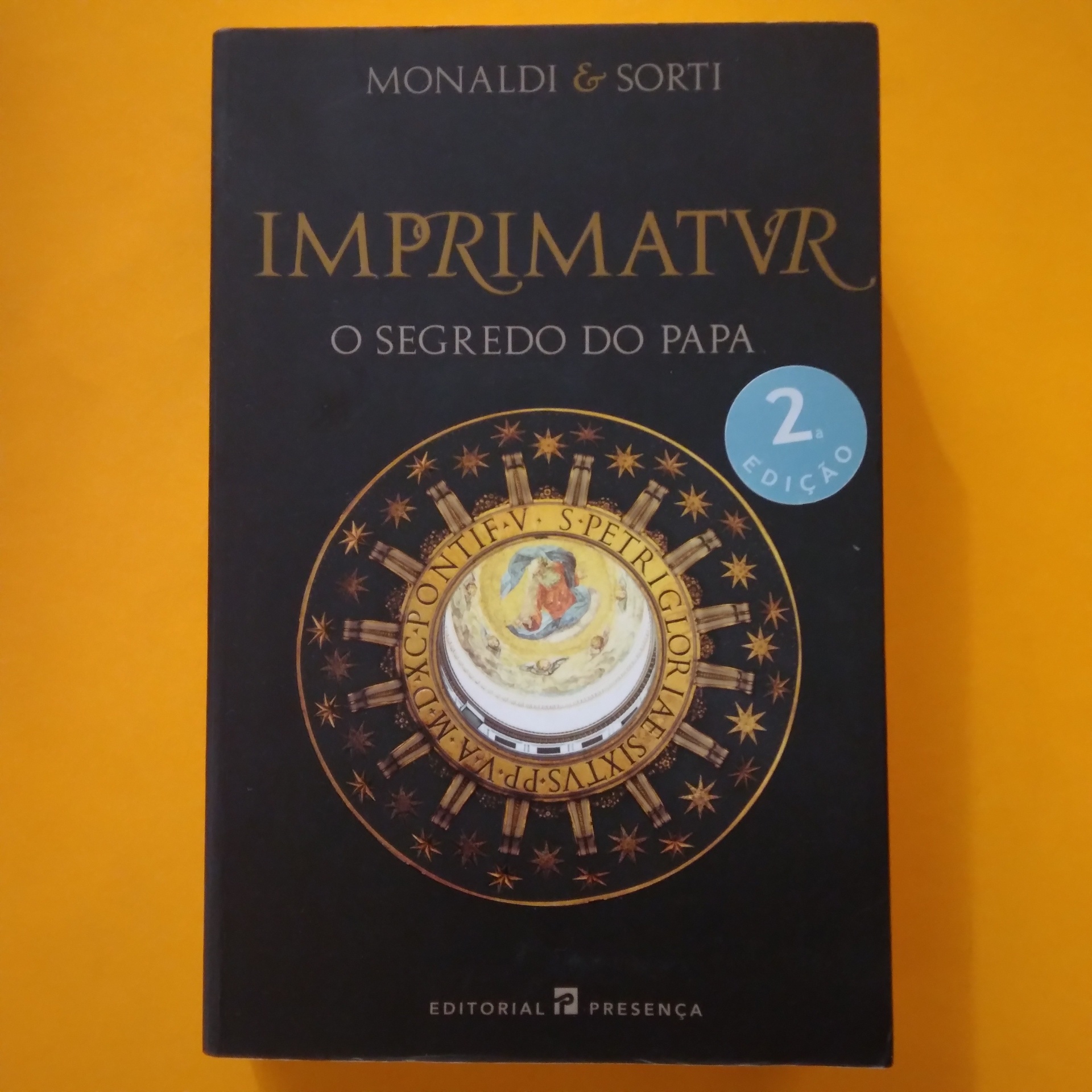 Imprimatur. O Segredo do Papa, Monaldi & Sorti Capa de livro preta com título dourado e selo azul, arte circular no centro, fundo amarelo.