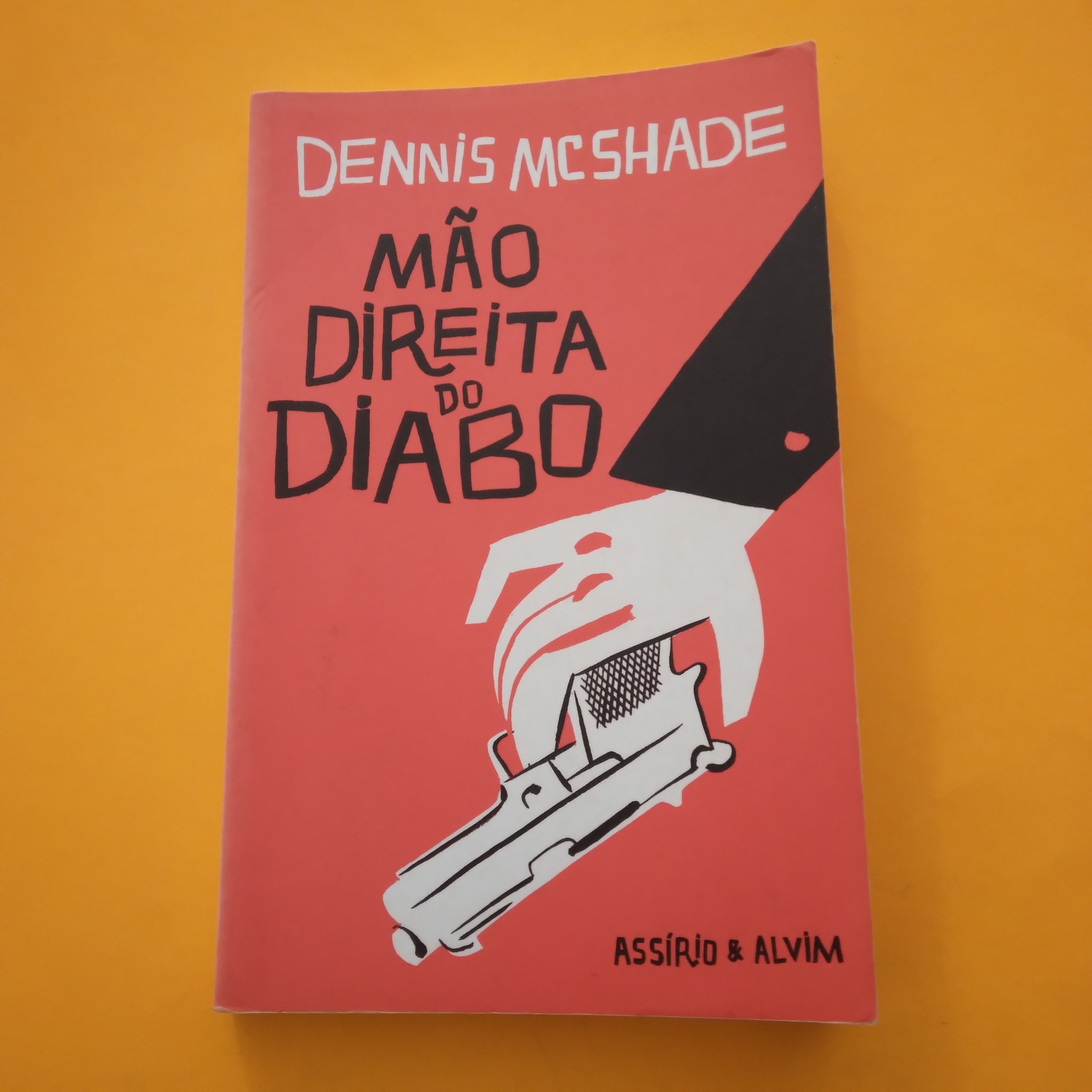 A Mão Direita do Diabo, Dennis McShade Livro vermelho com ilustração de mão segurando arma e texto na capa