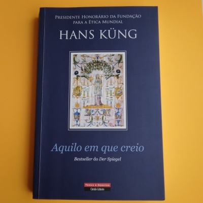 Livro com capa azul intitulado 'Aquilo em que creio' de Hans Küng sobre fundo amarelo