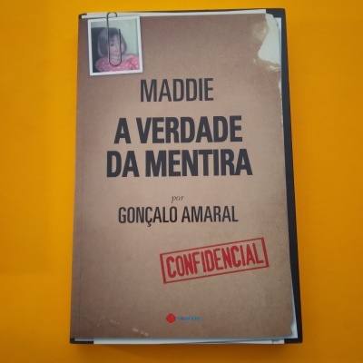Capa de livro castanha com texto preto e selo vermelho CONFIDENCIAL, foto presa por clipe, sobre fundo laranja