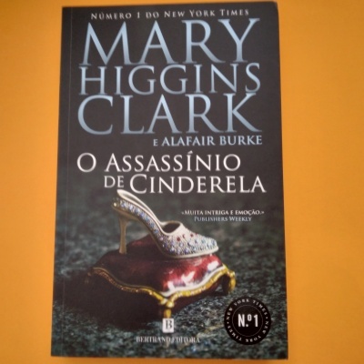 Capa do livro 'O Assassínio de Cinderela' com sapato de cristal sobre almofada vermelha