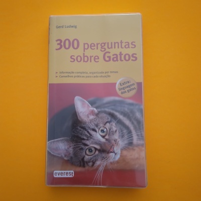Livro sobre gatos com foto de gato na capa, fundo bege e roxo