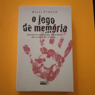 Livro 'o jogo de memória' de Nicci French com capa branca, título em preto e impressão de mão vermelha