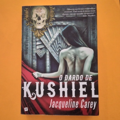 Capa do livro 'O Dardo de Kushiel' com mulher de costas e crânio decorativo