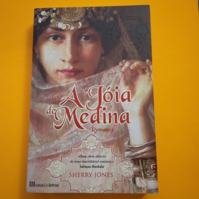 Capa do livro 'A Jóia de Medina' mostrando mulher com joias e véu em fundo amarelo