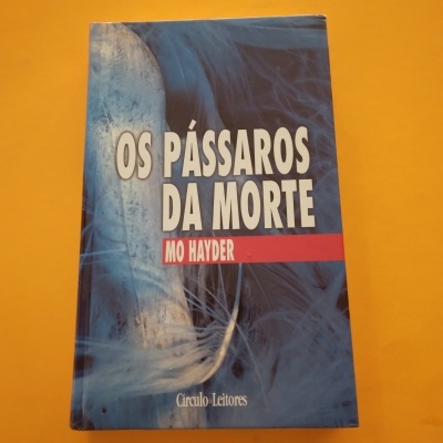 Livro 'Os Pássaros da Morte' de Mo Hayder com capa azul e branca e penas sobre fundo amarelo