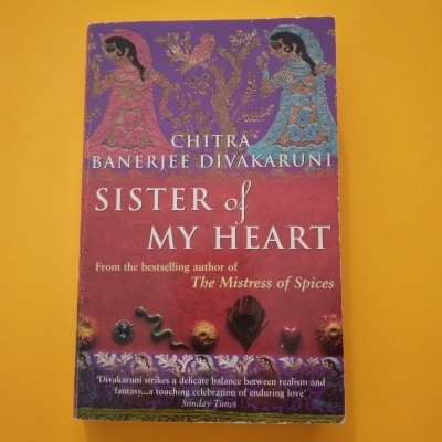 Capa do livro 'Sister of My Heart' com ilustrações decorativas douradas e cores vermelha e lilás