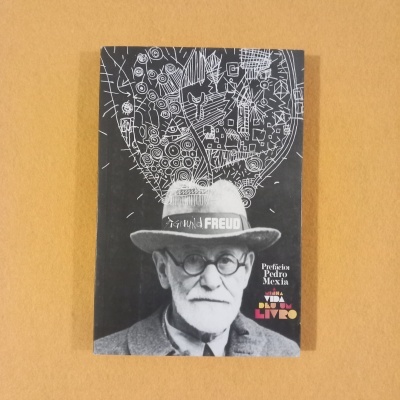 Capa de livro preto com foto de Freud e desenhos brancos acima do chapéu sobre fundo castanho