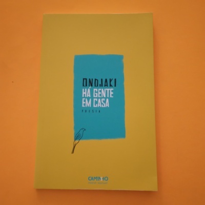 Livro amarelo com retângulo azul e texto ONDAKI HÁ GENTE EM CASA poema
