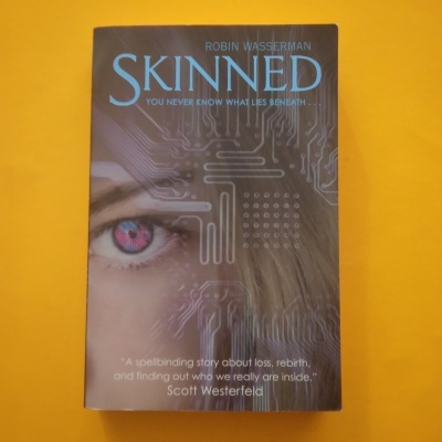 Capa do livro 'SKINNED' com olho rosa e circuito eletrónico
