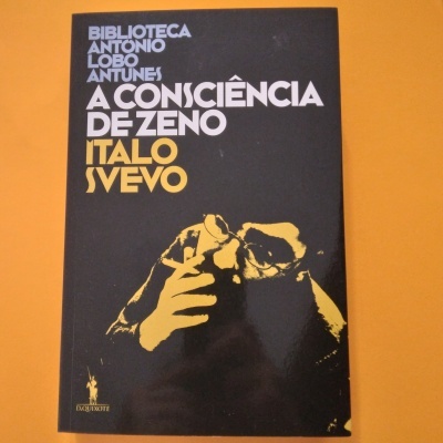 Livro com capa preta, texto branco e amarelo, imagem dourada de mão a segurar óculos