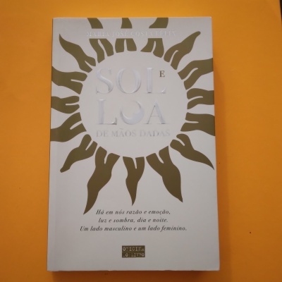 Livro com capa branca e desenho dourado de sol sobre fundo laranja