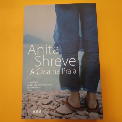 Capa do livro Anita Shreve A Casa na Praia com imagem de pessoa de chinelos em pedras