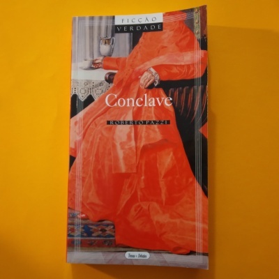 Livro 'Conclave' de Roberto Pazzi com capa vermelha e preta sobre fundo amarelo