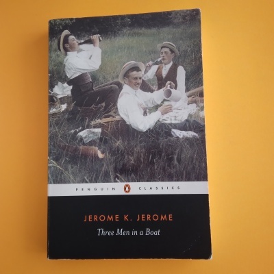 Capa do livro Three Men in a Boat de Jerome K. Jerome com foto vintage de três homens a beber numa relva