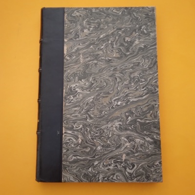 Livro capa dura marmoreada em cinza e bege com lombada preta sobre fundo amarelo