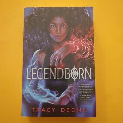 Capa do livro Legendborn de Tracy Deonn com mulher afro e efeitos de luz azul e vermelha nas mãos