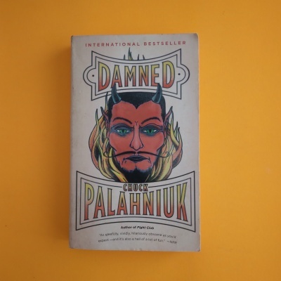 Livro 'Damned' de Chuck Palahniuk com capa ilustrada em fundo laranja