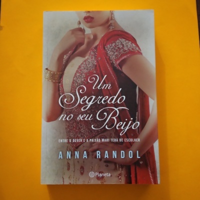 Livro 'Um Segredo no seu Beijo' com mulher em roupa tradicional vermelha e dourada sobre fundo amarelo