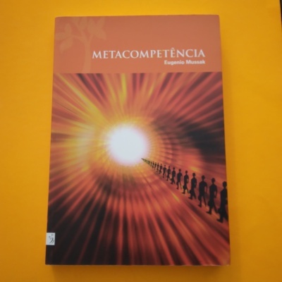 Capa de livro laranja e vermelha com título METACOMPETÊNCIA e figura humana em linha rumo a luz