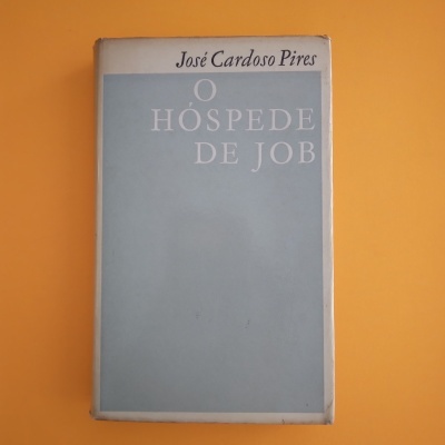 Livro 'O Hóspede de Job' de José Cardoso Pires com capa azul clara sobre fundo laranja