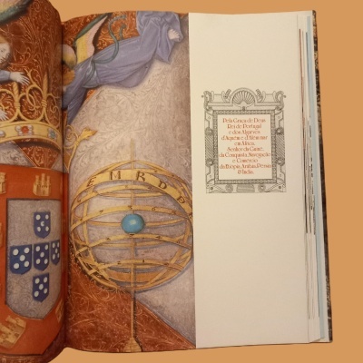 Livro aberto com ilustração de globo armilar, brasão e texto emoldurado