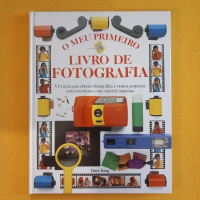 Livro 'O MEU PRIMEIRO LIVRO DE FOTOGRAFIA' com imagens de rolos de filme e acessórios fotográficos num fundo amarelo