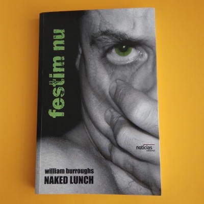 Capa do livro 'Naked Lunch' de William Burroughs com um olho verde destacado e mão cobrindo parte do rosto, texto verde e preto, fundo amarelo.