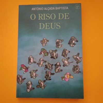 Capa de livro azul com título 'O RISO DE DEUS' e pessoas vistas de cima