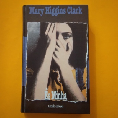 Capa de livro 'És Minha' de Mary Higgins Clark com imagem de mulher cobrindo o rosto.