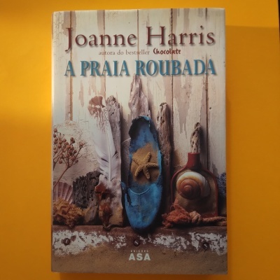Capa do livro A Praia Roubada de Joanne Harris com objetos naturais e fundo laranja.