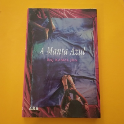 Livro 'A Manta Azul' com capa azul e vermelha mostrando duas pessoas deitadas em tecido azul