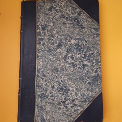 Livro com capa dura e padrão marmoreado sobre fundo laranja