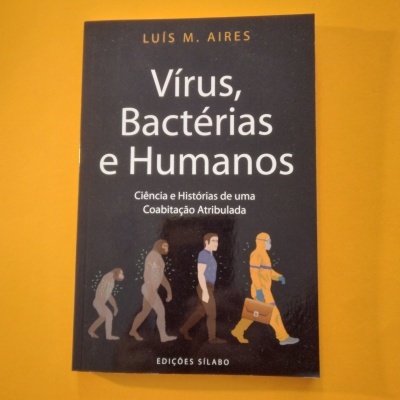 Livro 'Vírus, Bactérias e Humanos' sobre fundo amarelo