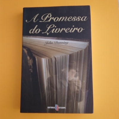 Capa do livro 'A Promessa do Livreiro' com imagem de páginas abertas sobre fundo amarelo